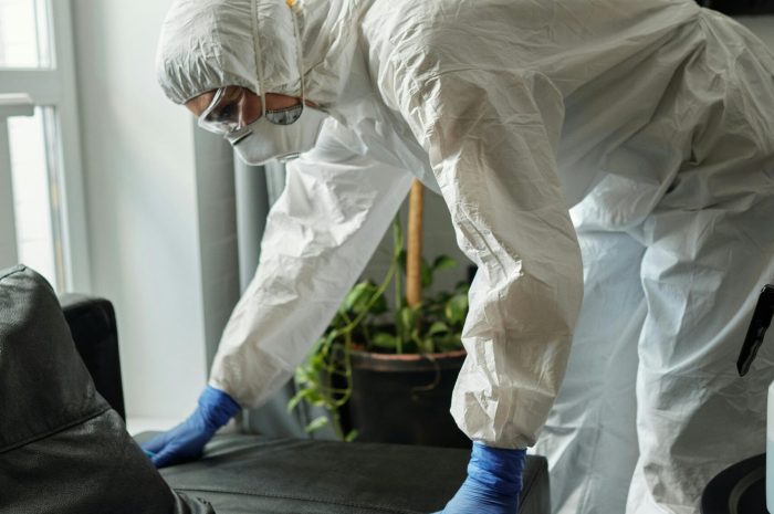 A person in full protective gear cleaning a modern living room, ensuring safety and hygiene.